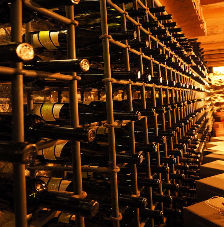stacked bottles on top of each other in the storage frame on the stone wall at Argyriou Winery